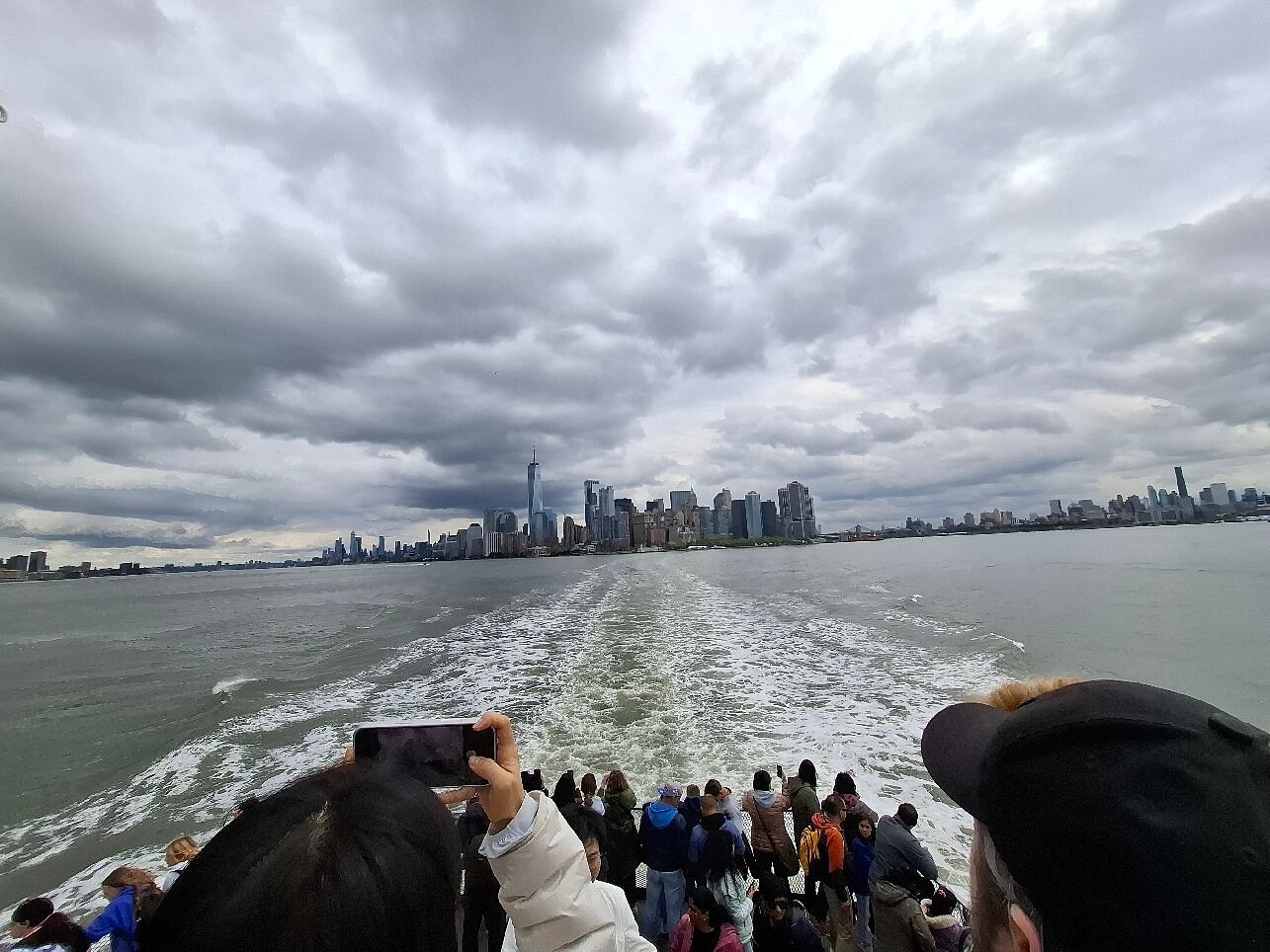 "Visitors aboard a Statue of Liberty ferry enjoy dramatic views of the Manhattan skyline, illustrating the best time to visit the Statue of Liberty in the morning versus sunset."