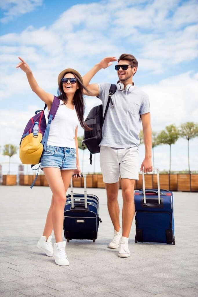 Two smiling travelers with backpacks and rolling suitcases walking outdoors, ready for their journey, representing travel preparation, sightseeing excitement, and exploring a new destination with confidence.