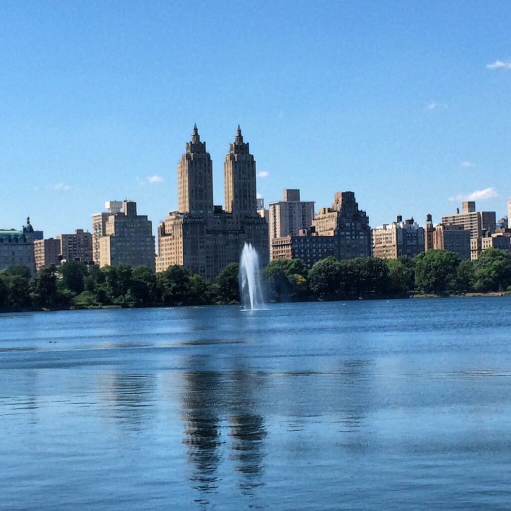 Scenic Central Park lake reflecting the Manhattan skyline and fountain, showcasing one of the best Central Park photo spots for visitors seeking picturesque landscapes, waterfront views, and iconic New York photography.