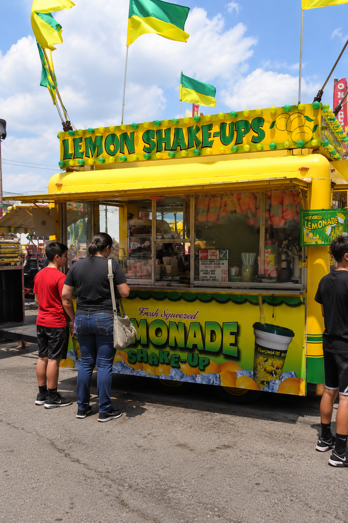 Bright yellow and green lemonade cart serves customers in Central Park, with colorful flags, fresh drinks, and sunny summer atmosphere.