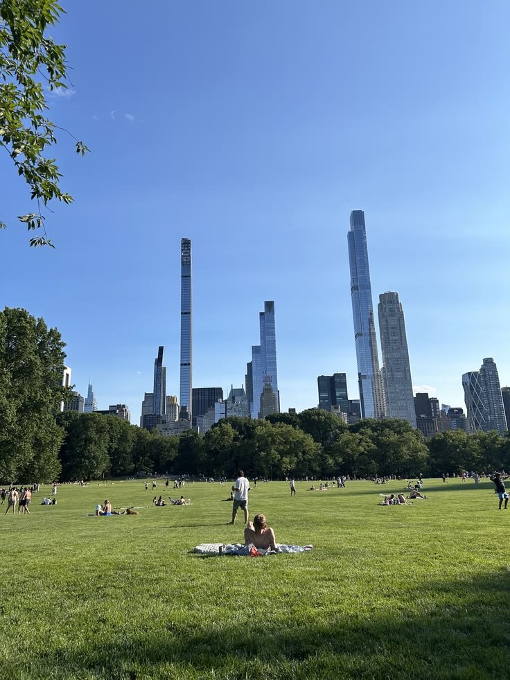 Visitors relax on the lush lawns of Sheep Meadow in Central Park, surrounded by towering Manhattan skyscrapers, open green space, sunny skies, and peaceful city views.