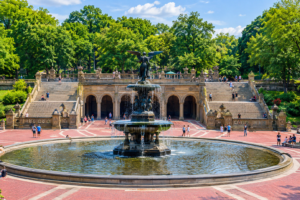 Bethesda Terrace and Fountain in Central Park, New York City, featuring ornate stone arches, broad staircases, a circular fountain, lush green trees, and visitors enjoying the scenic plaza.